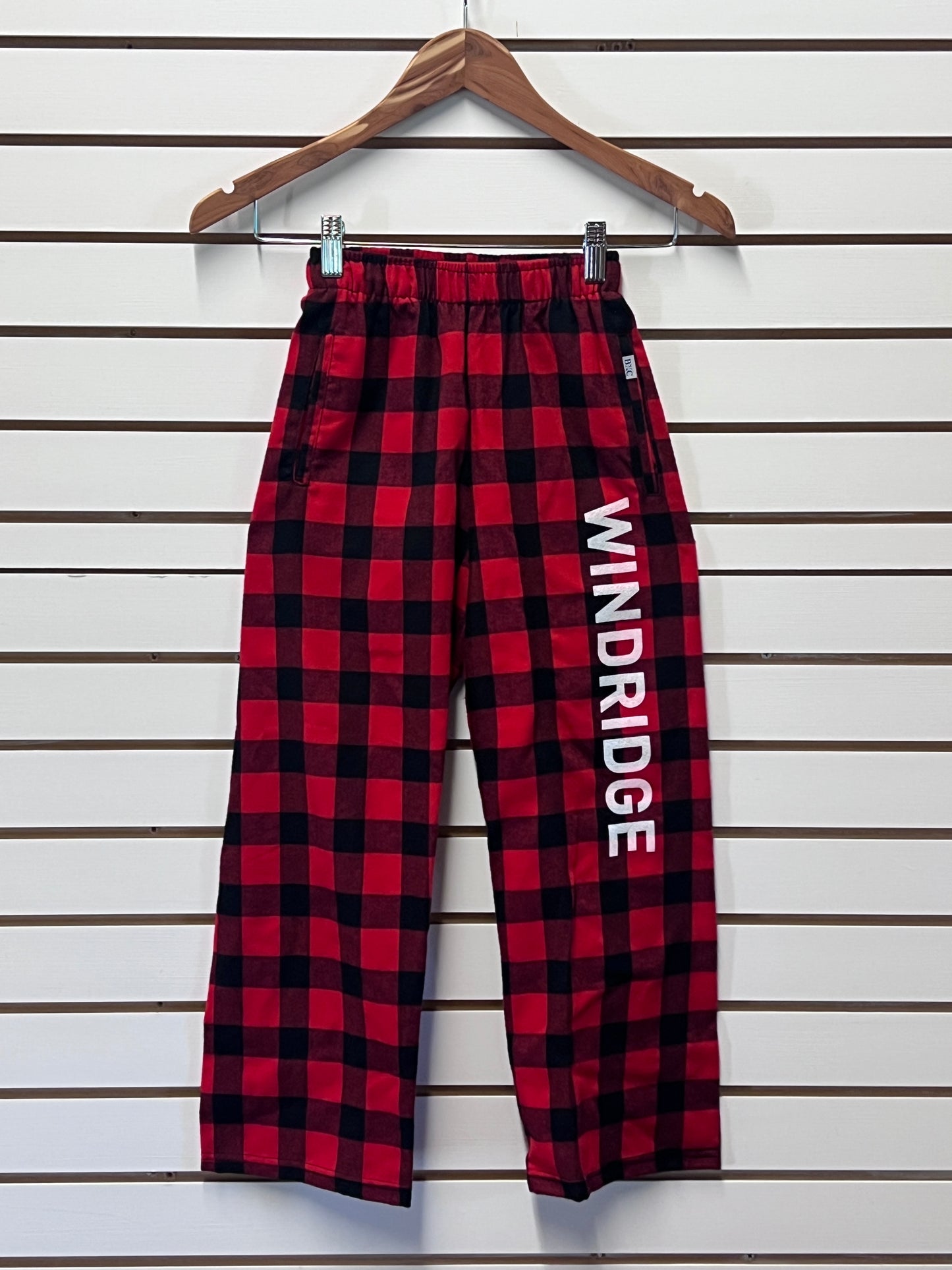 Red and black checkered pants with 'WINDRIDGE' branding on a wooden hanger against a white background.